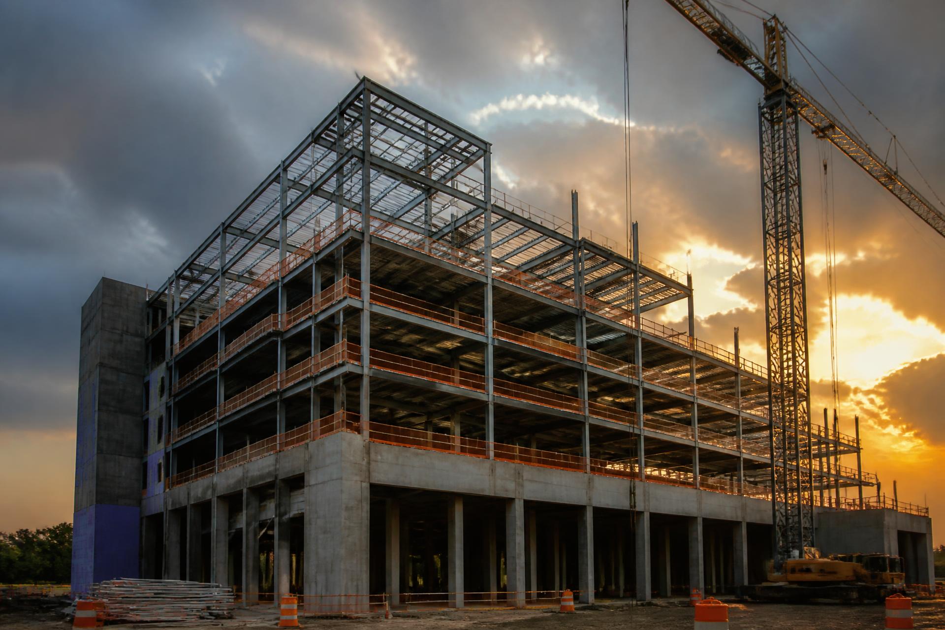 Commercial building under construction at golden hour with steel framing and a tower crane